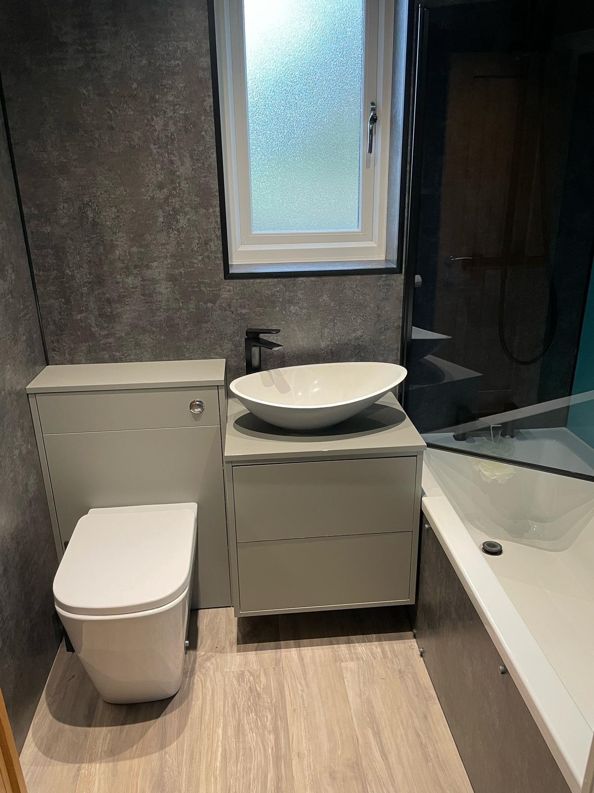 Modern bathroom with white toilet, floating vanity with round basin sink, and bathtub against textured gray walls